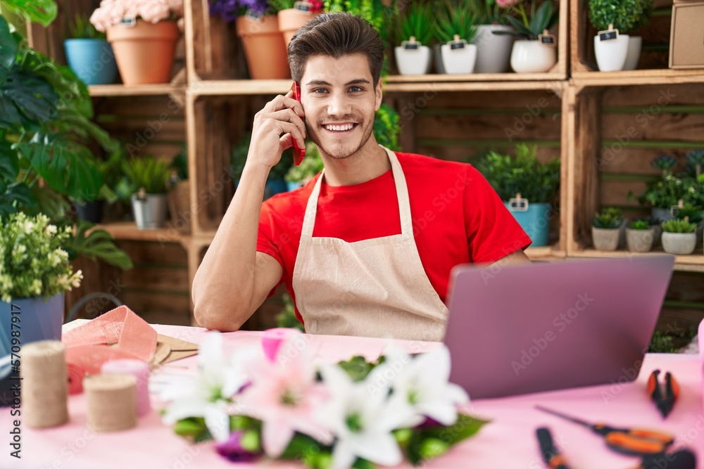 Young hispanic man florist talking on smartphone using laptop at flower shop Young hispanic man florist talking on smartphone using laptop at flower shop