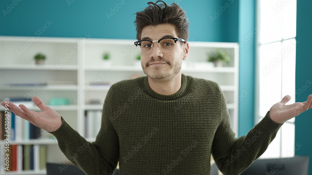 Young hispanic man student standing with i dont know expression at library university Young hispanic man student standing with i dont know expression at library university