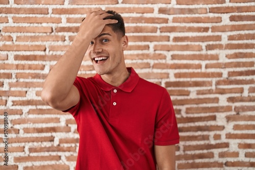 Young hispanic man standing over bricks wall surprised with hand on head for mistake, remember error. forgot, bad memory concept.