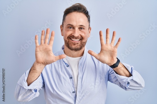 Middle age caucasian man standing over blue background showing and pointing up with fingers number ten while smiling confident and happy. © Krakenimages.com