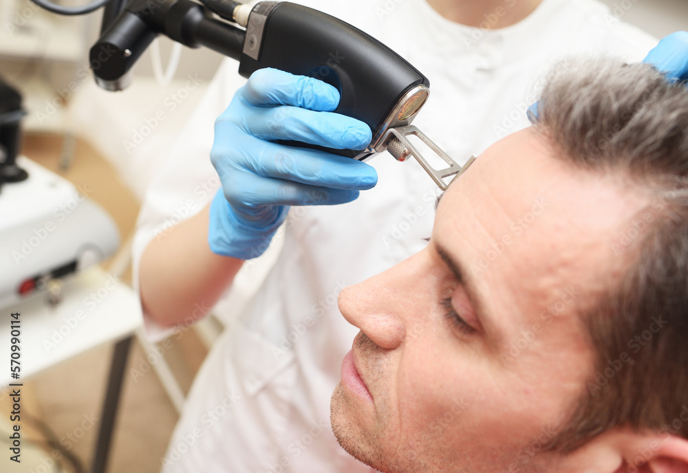 cosmetologist uses a CO2 fractional ablative laser to rejuvenate the skin of the face and remove vascular asterisks from a male patient in a modern cosmetic beauty clinic.