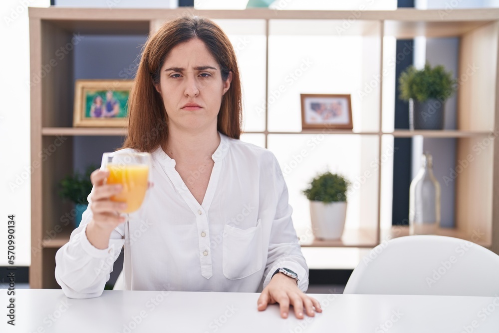 Brunette woman drinking glass of orange juice skeptic and nervous, frowning upset because of problem. negative person. Brunette woman drinking glass of orange juice skeptic and nervous, frowning upset because of problem. negative person.