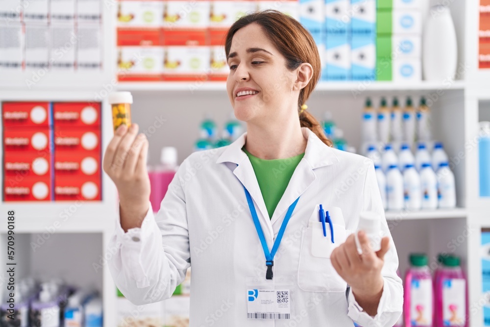 Young woman pharmacist smiling confident holding pills bottles at pharmacy Young woman pharmacist smiling confident holding pills bottles at pharmacy