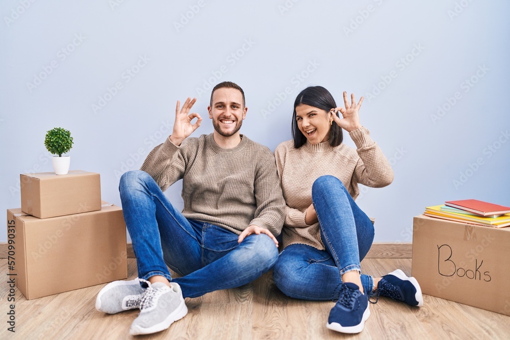 Young couple moving to a new home smiling positive doing ok sign with hand and fingers. successful expression. Young couple moving to a new home smiling positive doing ok sign with hand and fingers. successful expression.