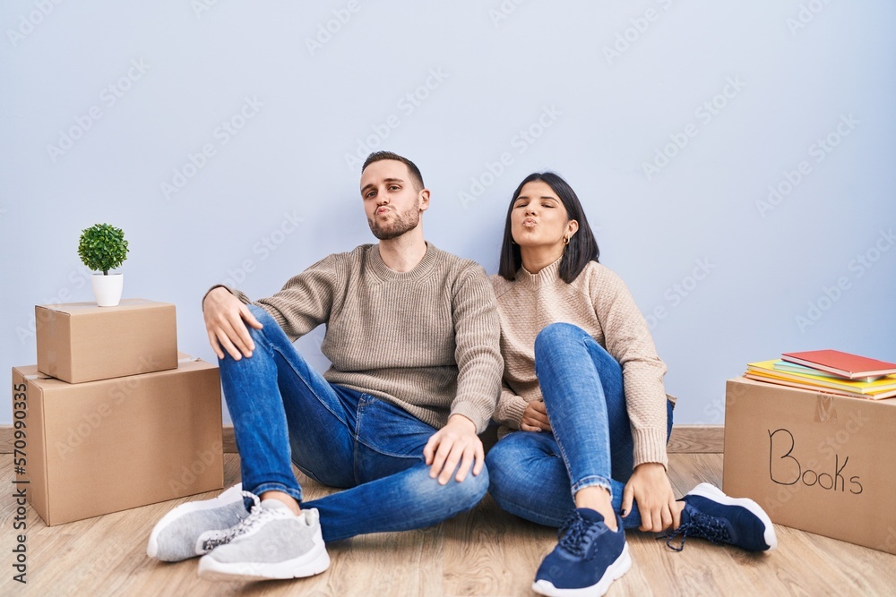 Young couple moving to a new home looking at the camera blowing a kiss on air being lovely and sexy. love expression. Young couple moving to a new home looking at the camera blowing a kiss on air being lovely and sexy. love expression.