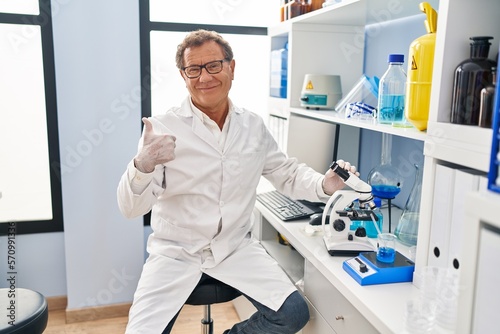 Senior man working at scientist laboratory smiling happy and positive  thumb up doing excellent and approval sign