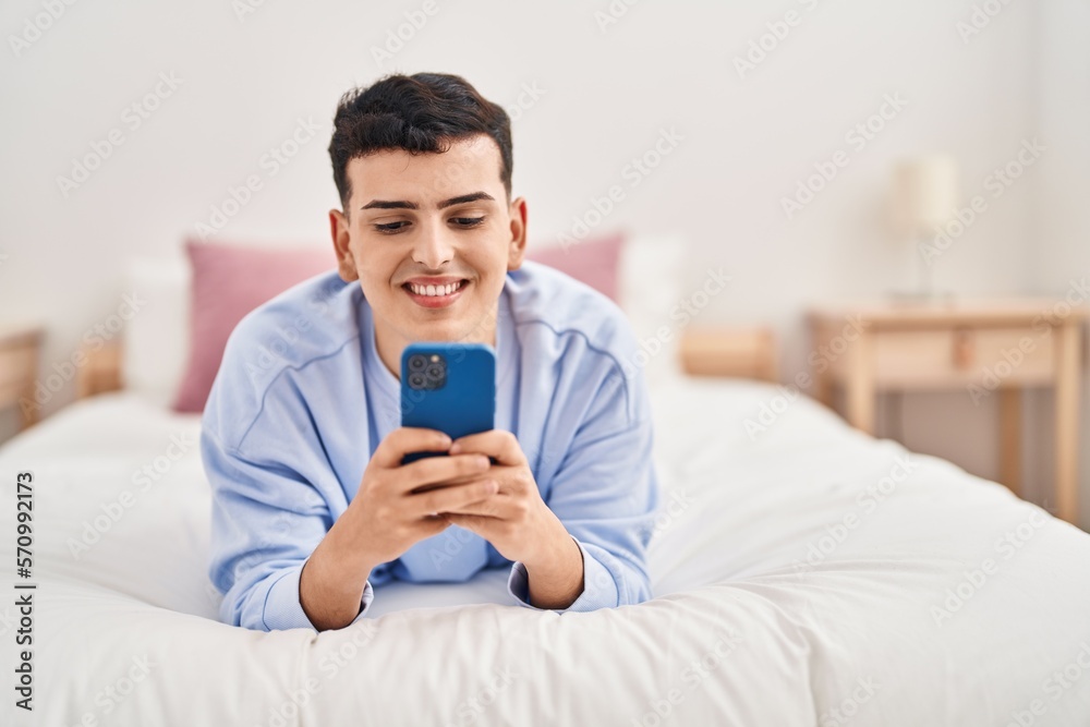 Young non binary man using smartphone lying on bed Young non binary man using smartphone lying on bed