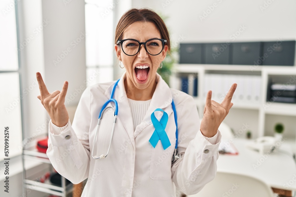 Young brunette doctor woman wearing stethoscope at the clinic shouting with crazy expression doing rock symbol with hands up. music star. heavy concept. Young brunette doctor woman wearing stethoscope at the clinic shouting with crazy expression doing rock symbol with hands up. music star. heavy concept.