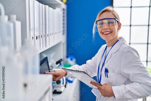 Young blonde woman scientist using computer reading document at laboratory