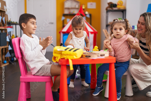 Teacher and group of kids sitting on table applauding at kindergarten