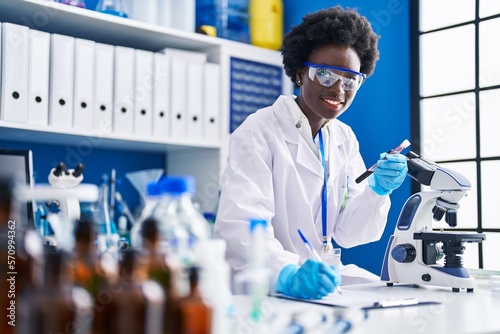 Young african american woman scientist writing on document holding blood analysis test tube at laboratory