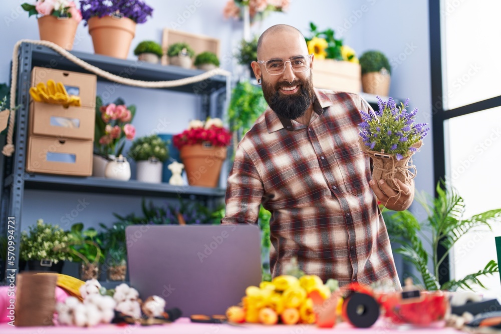 Young bald man florist using laptop holding plant at flower shop Young bald man florist using laptop holding plant at flower shop