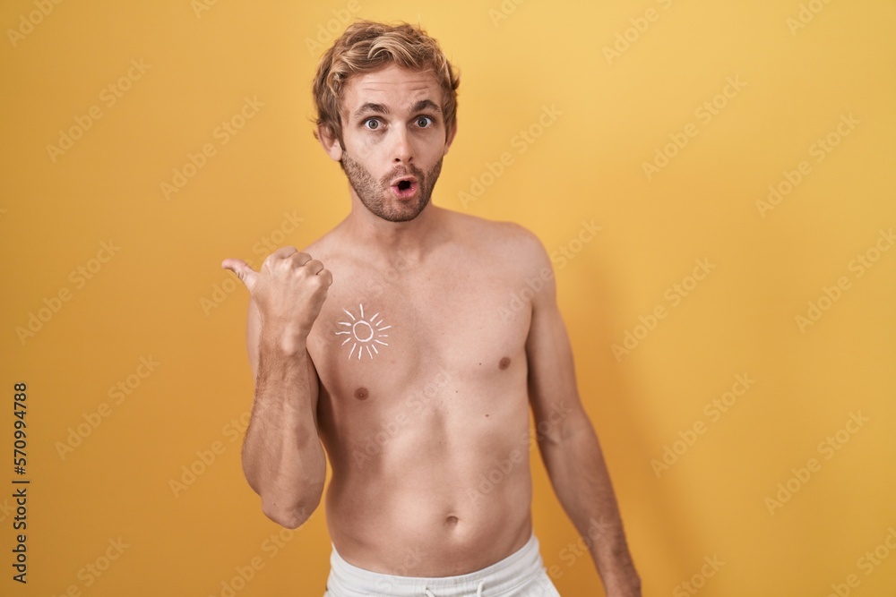 Caucasian man standing shirtless wearing sun screen surprised pointing with hand finger to the side, open mouth amazed expression.