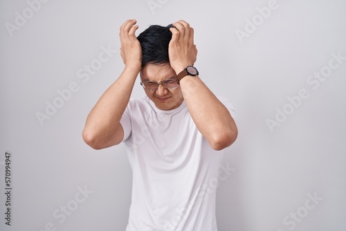 Foto Young asian man standing over white background suffering from headache desperate and stressed because pain and migraine