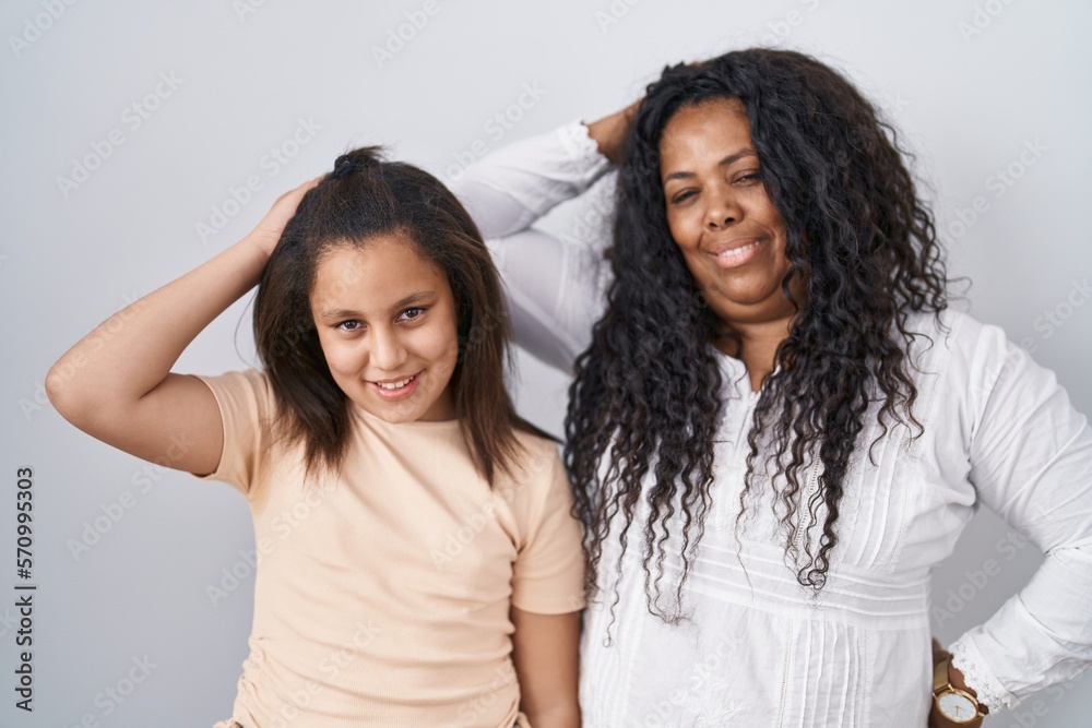 Mother and young daughter standing over white background smiling confident touching hair with hand up gesture, posing attractive and fashionable