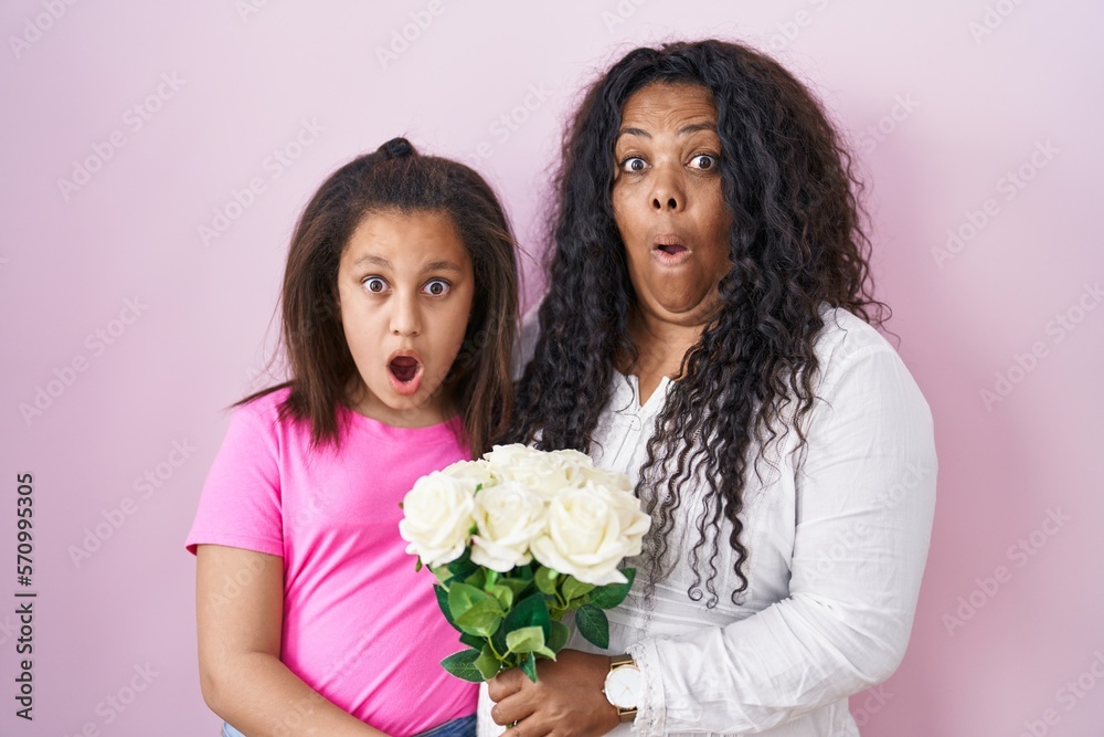Mother and young daughter holding bouquet of white flowers afraid and shocked with surprise and amazed expression, fear and excited face. Mother and young daughter holding bouquet of white flowers afraid and shocked with surprise and amazed expression, fear and excited face.