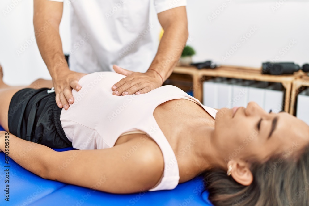 Obraz premium Latin man and woman wearing physiotherapist uniform having pregnancy rehab session massaging belly at physiotherapy clinic