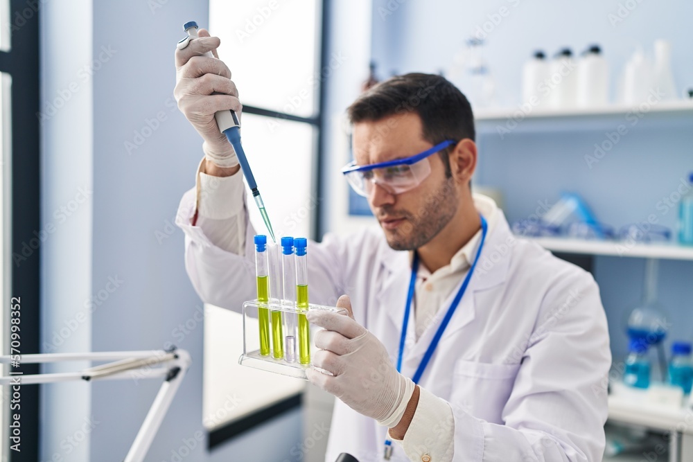 Young hispanic man scientist measuring liquid using pipette at laboratory Young hispanic man scientist measuring liquid using pipette at laboratory