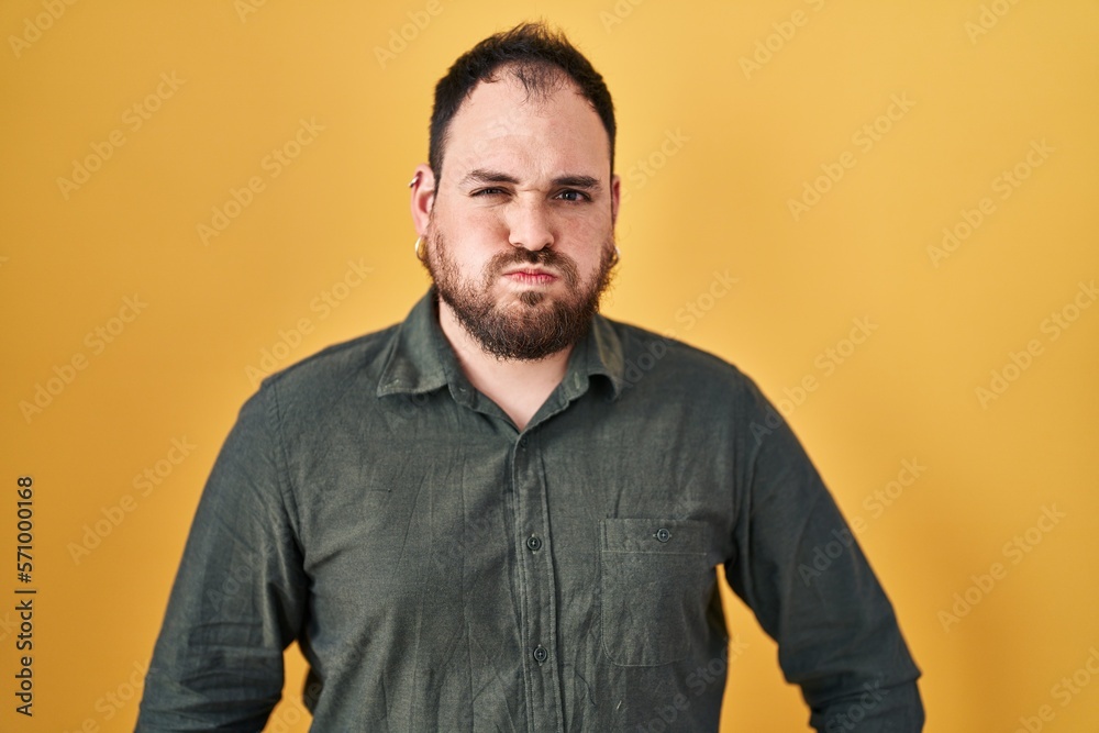 Plus size hispanic man with beard standing over yellow background puffing cheeks with funny face. mouth inflated with air, crazy expression. Plus size hispanic man with beard standing over yellow background puffing cheeks with funny face. mouth inflated with air, crazy expression.