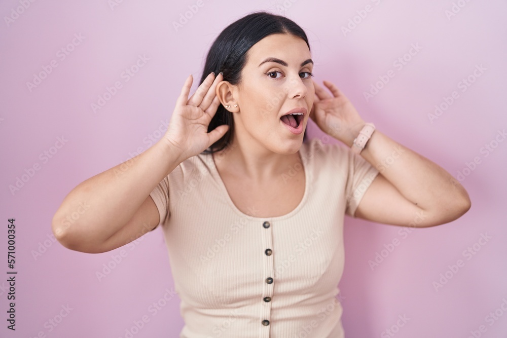 Young hispanic woman standing over pink background trying to hear both hands on ear gesture, curious for gossip. hearing problem, deaf Young hispanic woman standing over pink background trying to hear both hands on ear gesture, curious for gossip. hearing problem, deaf