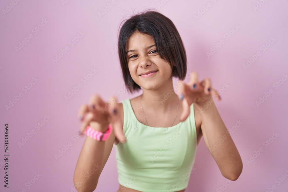 Young girl standing over pink background smiling funny doing claw gesture as cat, aggressive and sexy expression Young girl standing over pink background smiling funny doing claw gesture as cat, aggressive and sexy expression