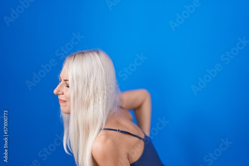 Caucasian woman standing over blue background suffering of backache, touching back with hand, muscular pain