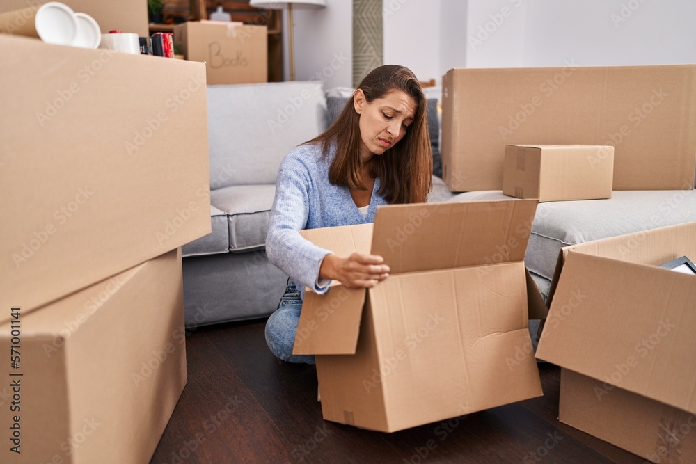 Young woman moving to a new home looking inside cardboard box depressed and worry for distress, crying angry and afraid. sad expression. Young woman moving to a new home looking inside cardboard box depressed and worry for distress, crying angry and afraid. sad expression.