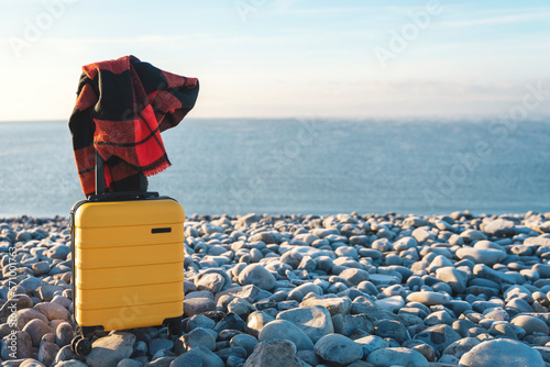 Yellow Suitcase with an orange scarf on the seaside against the sea. Travel concept. © Iryna