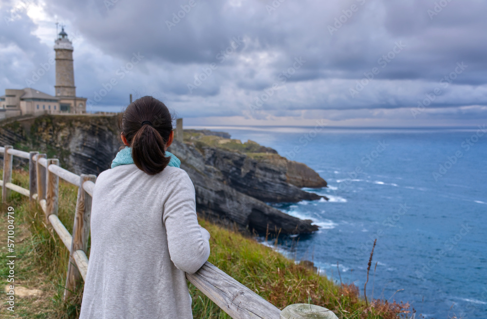 Mujer contemplando el mar un día nublado, un faro en Santander España.