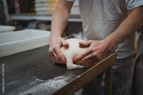 Anonymous baker man kneading bread dough on metal table in a bakery photo