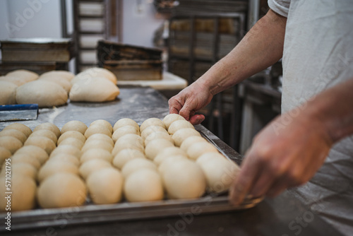 Baker man holding a metal tray full of balls of bread dough in kitchen of bakery