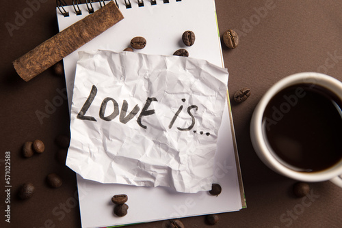 The inscription love is and a notebook with a cup of coffee