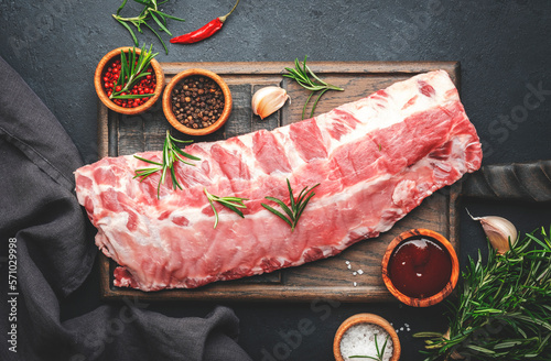 Raw pork ribs with rosemary and spices on rustic wooden cutting board prepared for cooking on black kitchen table background, top view
