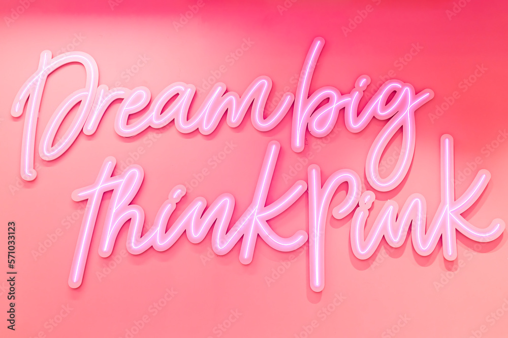 Bright pink neon sign saying dream big and think pink on red wall