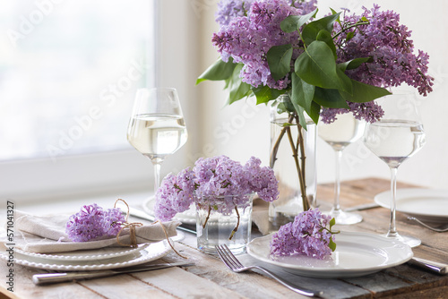 Beautiful table decor for a wedding dinner with a spring blooming lilac flowers. Celebration of a special holiday marriage event. Fancy white plates  wineglasses. Countryside style