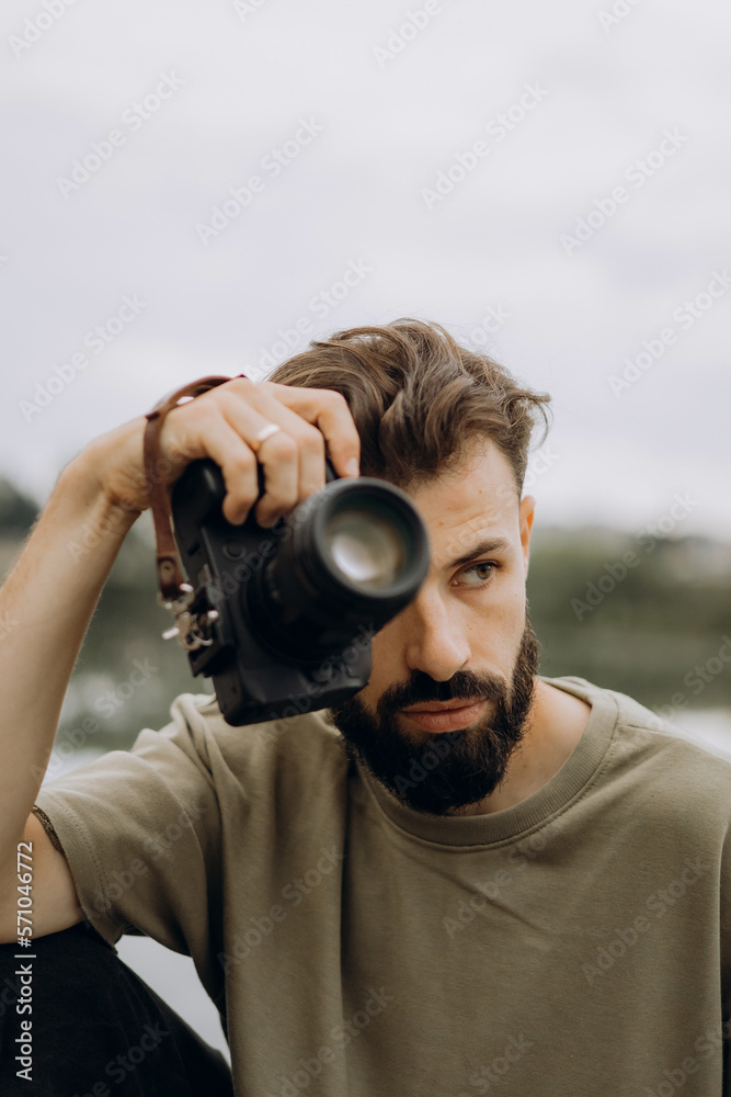 Obraz premium a young man with a modern SLR camera in his hands on a natural background