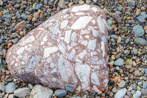 A closeup of a well weathered conglomerate rock on a beach. The rock is rounded and worn, and is composed many smaller rocks.