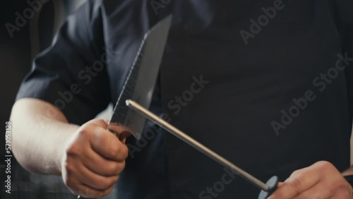 Slow motion close-up video of a chef sharpening a knife in the kitchen. A professional prepares knives for slicing food to prepare meals for restaurant visitors.