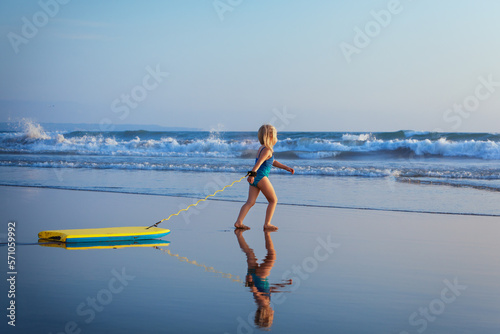 Little baby girl - young surfer with bodyboard has fun on sea beach. Family lifestyle, people outdoor water sport lessons and swimming activity on summer vacation with child in adventure surf camp.