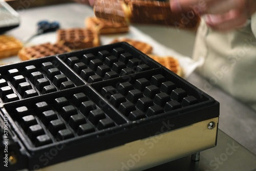 Close-up chef pours waffle batter in a waffle iron in a professional kitchen. Waffle making at the hotel with all-inclusive meals. belgian waffles in a waffle iron.