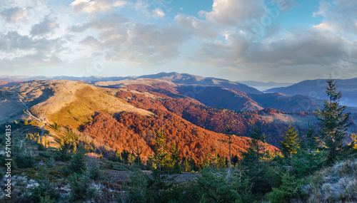 Sunrise in autumn Carpathian. Mountain top daybreak landscape with colorful trees on slope.