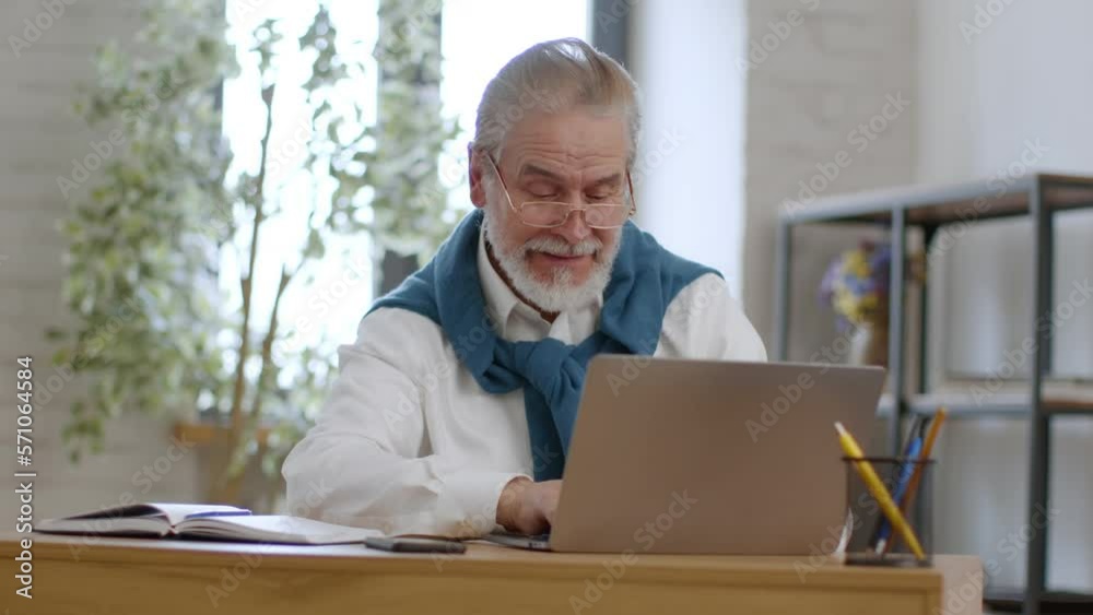 Positive retirement. Cheerful senior grey haired man in eyeglasses web surfing online on laptop computer, free space Positive retirement. Cheerful senior grey haired man in eyeglasses web surfing online on laptop computer, free space