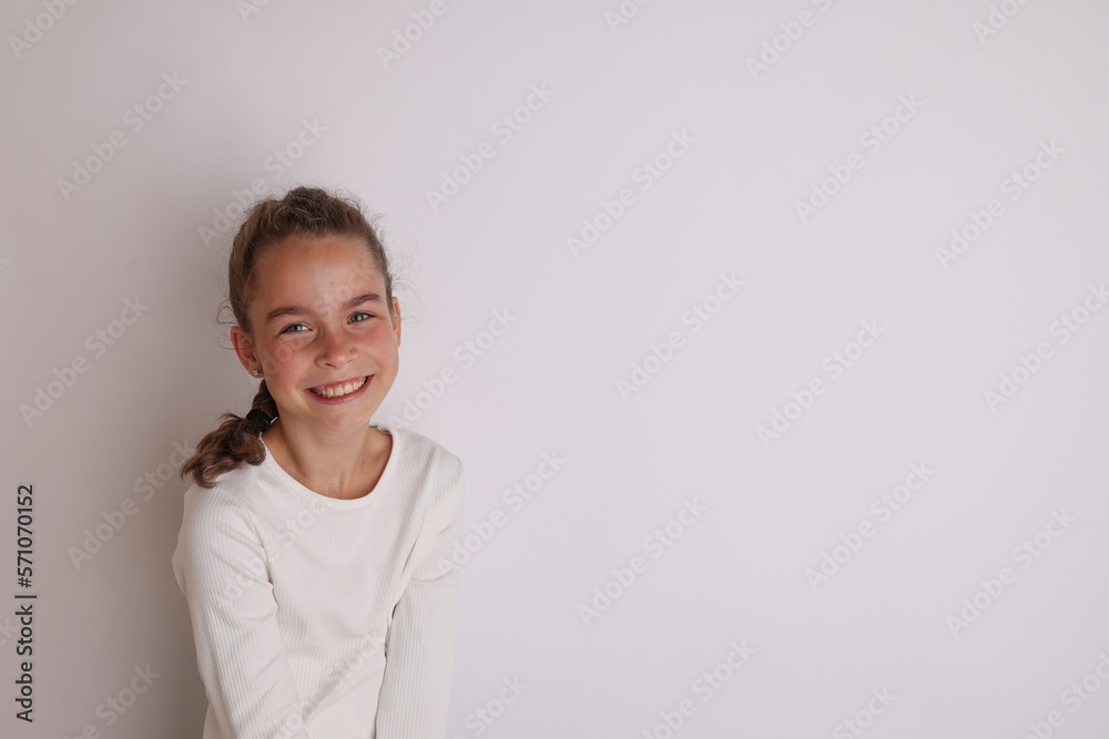 Little emotional teen girl in white shirt 11, 12 years old on an isolated white background. Children's studio portrait. Place text, to copy space for inscription, advertising children's goods.