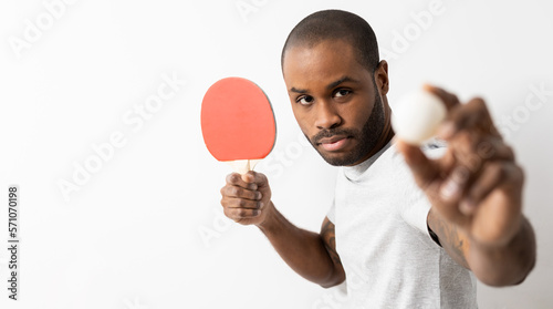 A dark-skinned adult man posing on a white background with a ping.pong racket and a ball. Concept of ping-pong player. photo