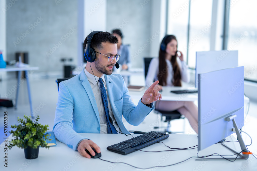 Handsome male operator with headset in blue suit working on computer in call center. Handsome male operator with headset in blue suit working on computer in call center.