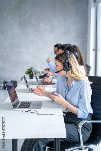 Vertical side view of beautiful blond hair call canter agent working with group of operators in office