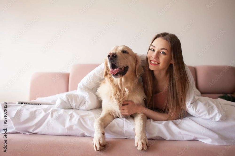 young girl lies on a bed with a golden retriever dog and smiles, a woman with pet rest at home young girl lies on a bed with a golden retriever dog and smiles, a woman with pet rest at home