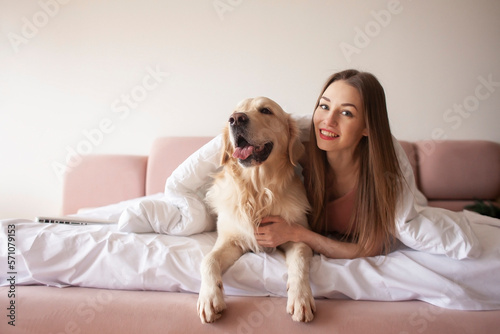 young girl lies on a bed with a golden retriever dog and smiles, a woman with pet rest at home