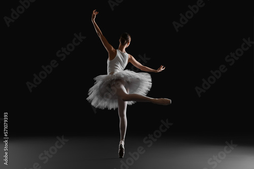 Young ballerina practicing dance moves on black background