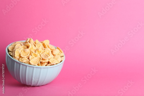 Bowl of tasty crispy corn flakes on pink background, space for text